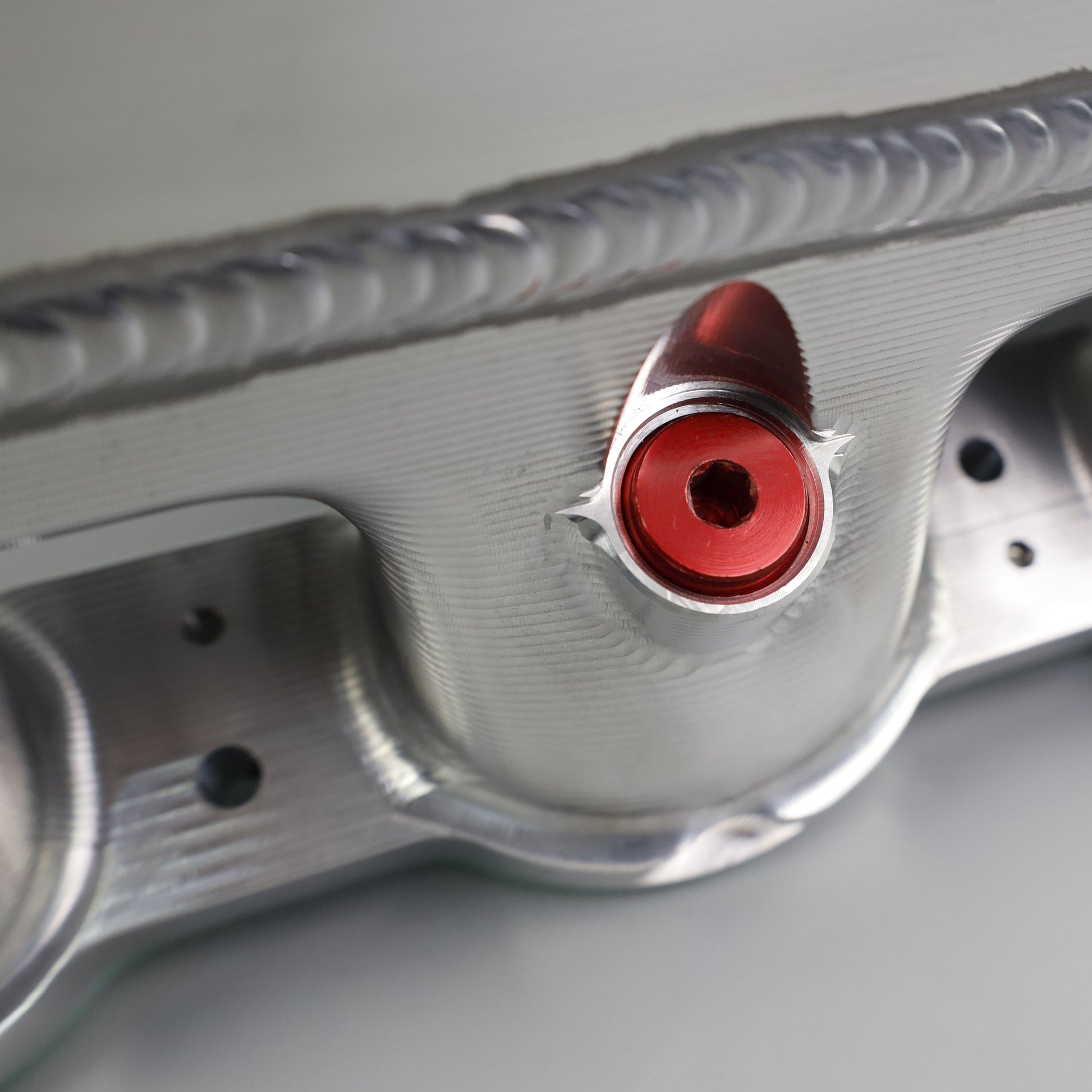 Close-up of a metallic engine valve cover with red bolts on a gray background